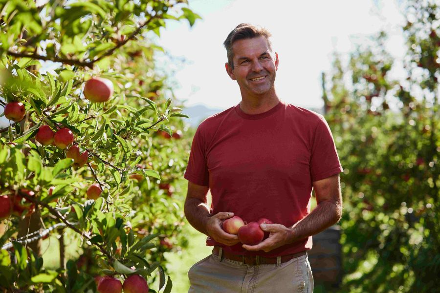 Andrew Smith wears a red tshirt in an apple orchard